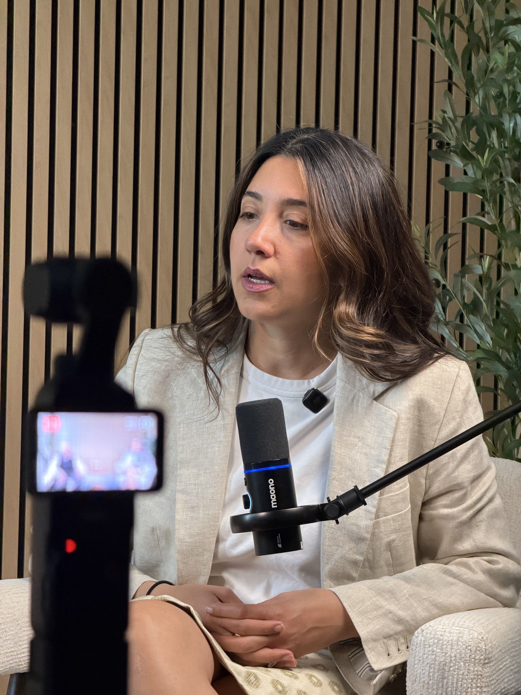A guest in a linen blazer talking into a microphone while a camera records at Axeom Content Studio