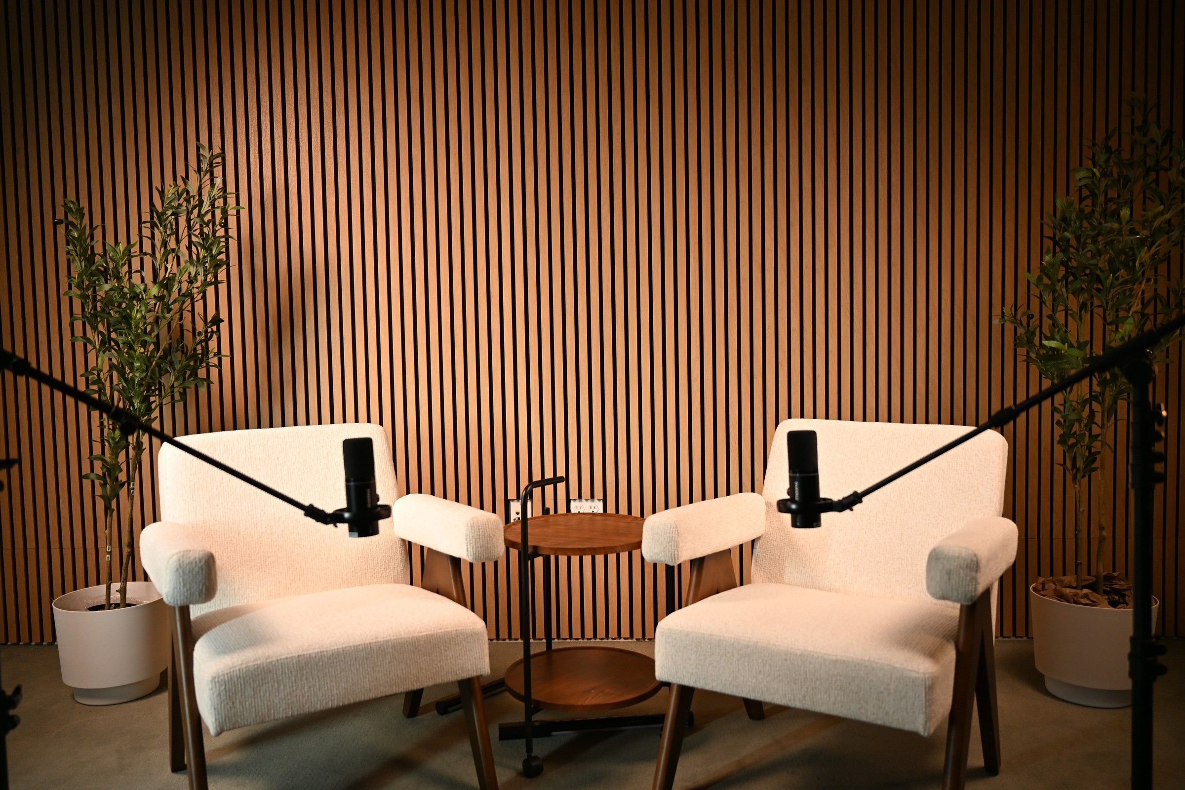The empty podcast set at Axeom Content Studio in Dallas, Texas: two cream chairs, microphones on boom arms, a slatted wood wall