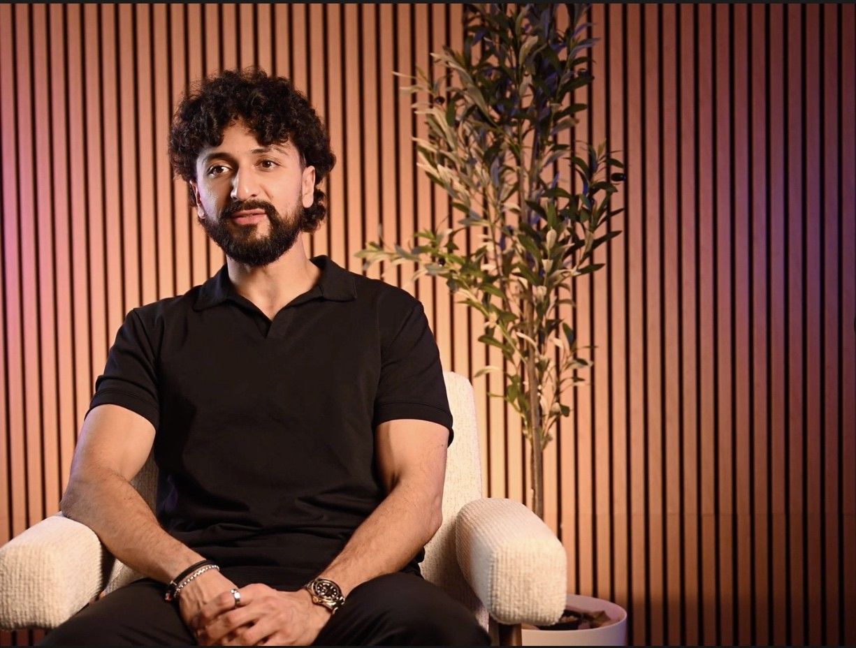 A man in a black polo seated in a cream chair, facing the camera, at Axeom Content Studio
